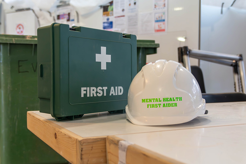 A first aid kit and a hard hat with the words "Mental Health First Aider" written on it.