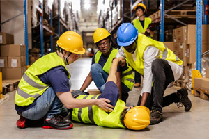A warehouse worker collapsed on the floor, while his colleagues tend to him.