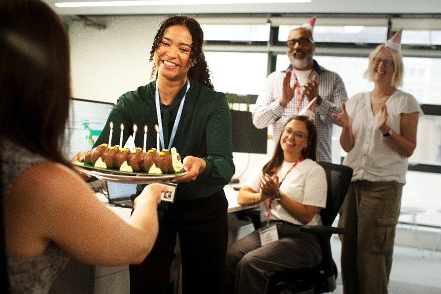 An office worker presenting a birthday cake to her colleague.
