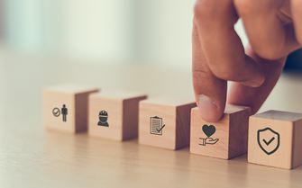 An arrangement of small blocks on a table, with illustrations on one side of each. A hand is gesturing towards one with a health related illustration.