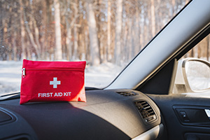 A first aid kit atop of the dashboard of a car, in a winter setting.