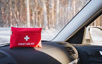 A first aid kit atop of the dashboard of a car, in a winter setting.