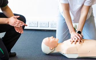 A woman taking instructions from a St John Ambulance trainer about chest compressions.