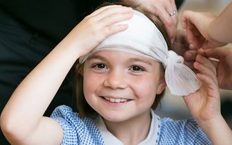 A child in her school uniform with a bandage wrapped around her head. A child in her school uniform with a bandage wrapped around her head.
