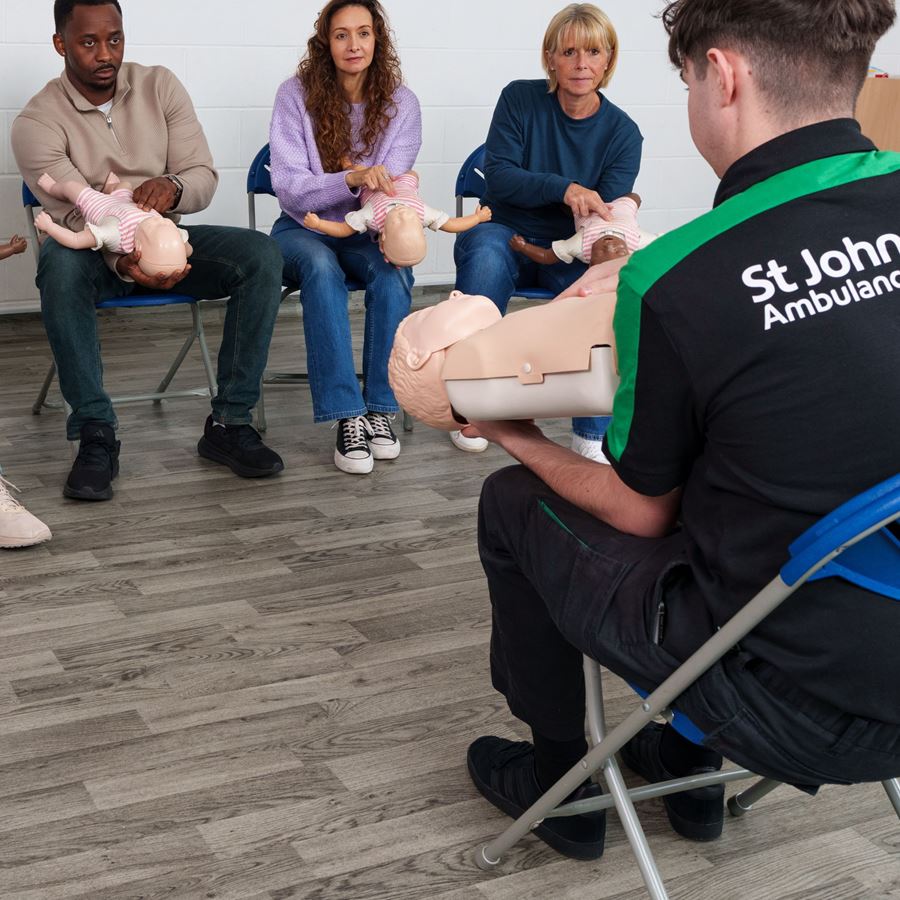 First Aid Trainer showing four people how to do baby CPR on a mannequin.