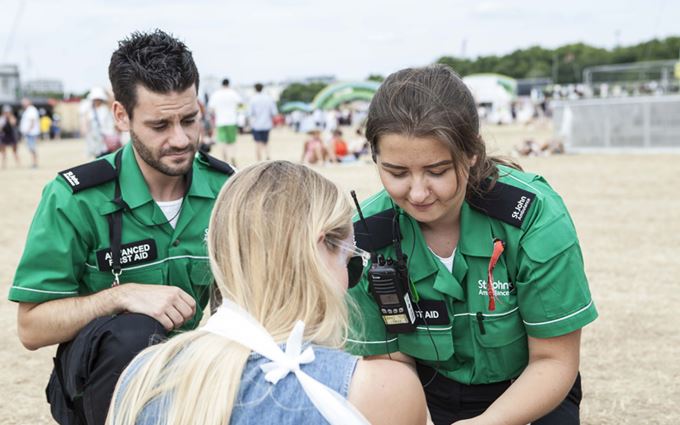 Two SJA first aiders help a patient with her arm in a sling at event