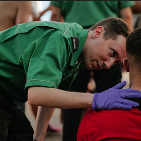 A volunteer putting their hand on the shoulder of a man sitting down. A volunteer putting their hand on the shoulder of a man sitting down.