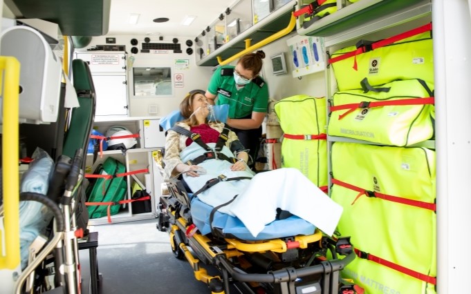 St John Ambulance volunteer standing and a patient strapped into a stretcher in the back of an ambulance.