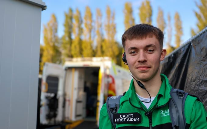 A Cadet First Aider wearing an earpiece in front of an ambulance.