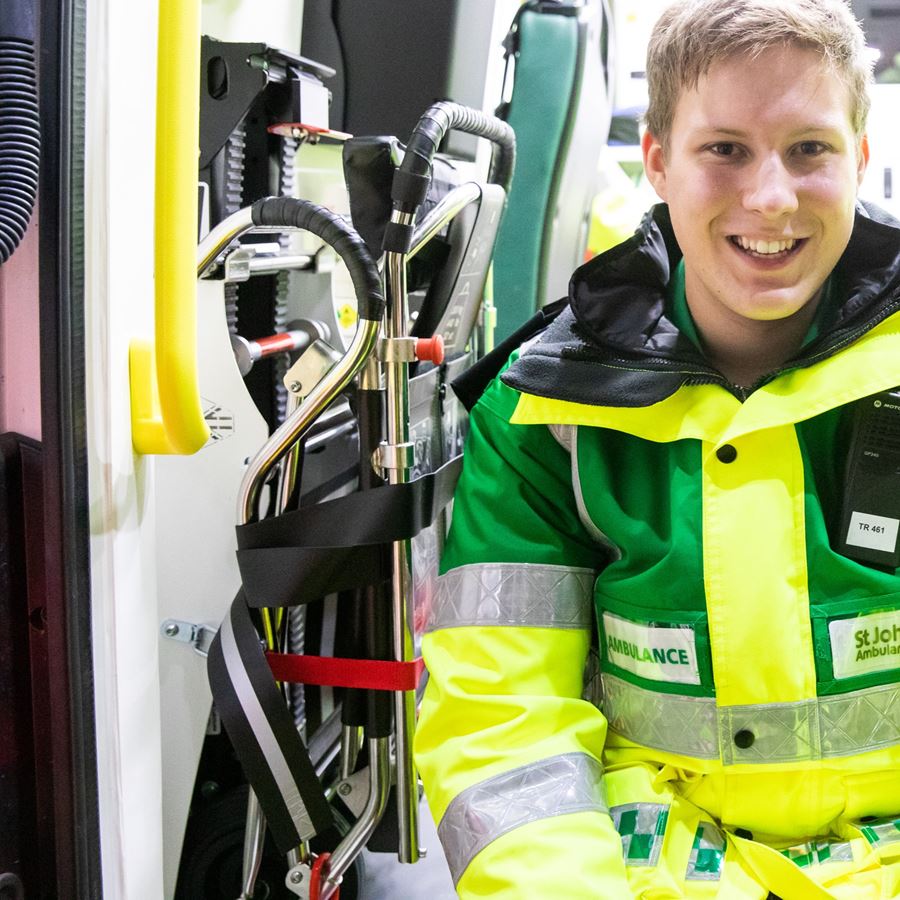 A smiling volunteer wearing a high vis uniform jacket sat in the back of an ambulance.