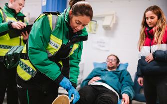 A patient is lying down on a bed being treated by a first aid volunteer. Another volunteer is stood looking at a folder. 
