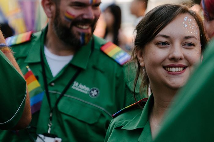 Two volunteers in St John Ambulance uniform, smiling, with glitter on their face and rainbow flags on their cheeks.