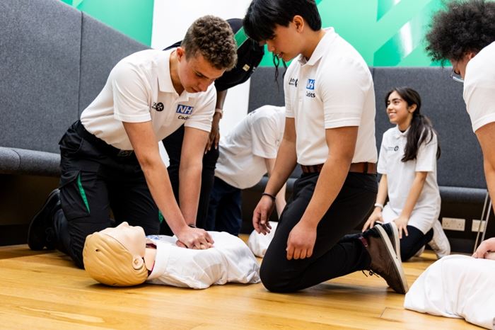 Two NHS Cadets kneeling on the floor with one practising chest compressions on a mannequin.