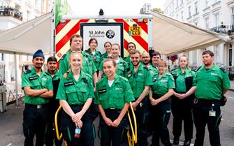 Large group of smiling volunteers standing in front of an ambulance.