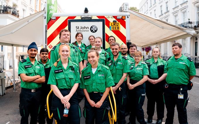 Large group of smiling volunteers standing in front of an ambulance.
