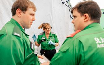 A photo of St John Ambulance volunteers. In the foreground, two male volunteers are talking, while in the centre of the background, a female volunteer is laughing.