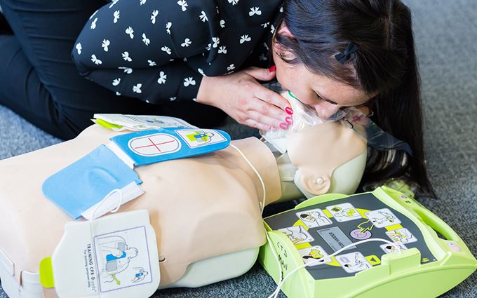 Woman practicing CPR and using a defibrillator on a training manikin.