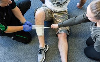 Trainer demonstrates how to apply a bandage to a leg wound during a first aid course. 