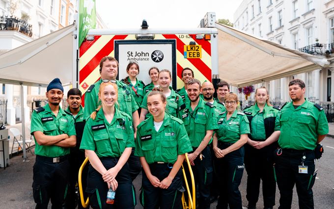 A group of 15 St John Ambulance first aider volunteers standing in front of an ambulance.