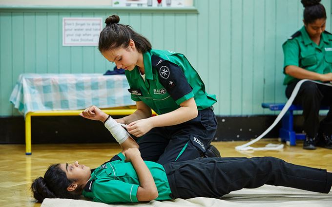 2 cadets practising bandaging an arm. 