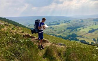Duke of Edinburgh expedition participant looking at a map surrounded by countryside.