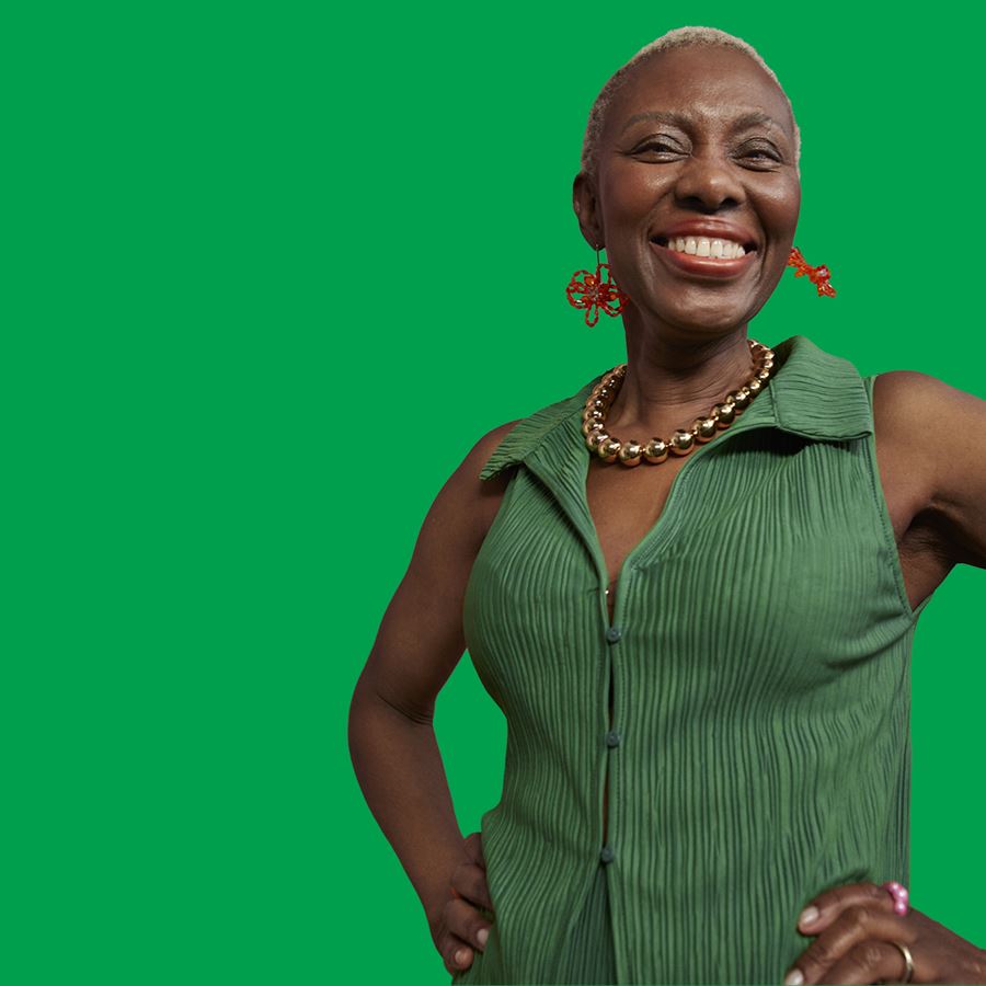 Woman wearing a green top and red earrings standing with her hands on her hips smiling, in front of a green background.