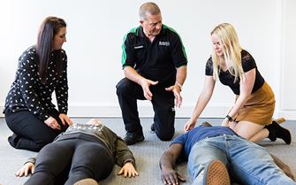 First aid course participants learning how to put someone in the recovery position First aid course participants learning how to put someone in the recovery position